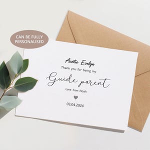 Può includere: Un biglietto bianco con il testo "Zia Evelyn, Grazie per essere il mio Guide parent, Love from Noah, 03.04.2024." Una busta marrone è dietro il biglietto. Le parole "PUÒ ESSERE COMPLETAMENTE PERSONALIZZATO" sono in un cerchio in alto a sinistra.
