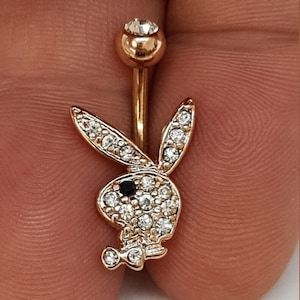 Puede incluir: Anillo para el ombligo de color dorado con un diseño de logotipo de conejito. El conejito está incrustado con cristales transparentes, con un ojo de cristal negro. Las bolas superior e inferior también están adornadas con cristales. Una joya corporal elegante.