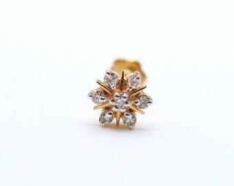 May include: A gold-toned stud earring with a floral design. The earring features a central cluster of small, clear gemstones surrounded by six larger gemstones, creating a starburst effect. The earring is set against a white background.