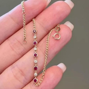 May include: A gold bracelet with alternating ruby and diamond stones. The bracelet has a chain design and a lobster clasp. The gemstones are set in a row, creating a classic and elegant look. The bracelet is shown against a neutral background.