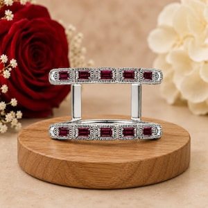 Peut inclure: Une bague double en métal argenté composée de deux rangées parallèles de pierres précieuses rectangulaires rouge foncé. Les bandes métalliques présentent une texture milgrain sur les bords, reliées par deux barres verticales argentées.