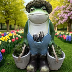 Puede incluir: Una estatua caprichosa de una rana de jardín con sombrero de paja, peto azul y botas negras. La rana sostiene dos cubos blancos con plantas. Una pequeña pala y un tenedor están en el bolsillo. La estatua está en un jardín con flores coloridas.