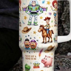 May include: A white travel mug featuring characters from the animated film "Toy Story." The design includes Buzz Lightyear, Woody, Jessie, and other characters, along with the phrases "To Infinity and Beyond" and "You've Got a Friend in Me."