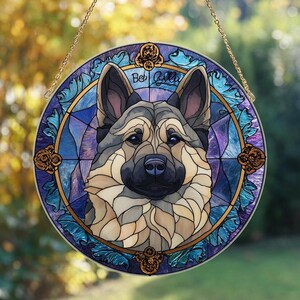 May include: Round stained glass window featuring a German Shepherd dog. The artwork uses shades of blue, purple, and tan, with gold accents. The dog's name, "Bel Gilli", is written in script. A gold chain is attached for hanging.