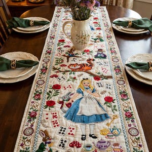 May include: A cream-colored quilted table runner featuring embroidered Alice in Wonderland characters including Alice, the White Rabbit, and the Cheshire Cat, surrounded by playing cards, red roses, teapots, and a floral border with clocks.