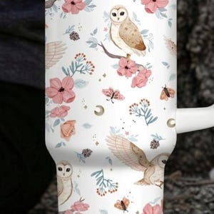 Puede incluir: Taza de viaje blanca con un dise&ntilde;o envolvente con b&uacute;hos, flores rosas y mariposas. La taza tiene un asa y una tapa blancas y es adecuada para bebidas fr&iacute;as o calientes. La taza mide aproximadamente 18 cm de alto.