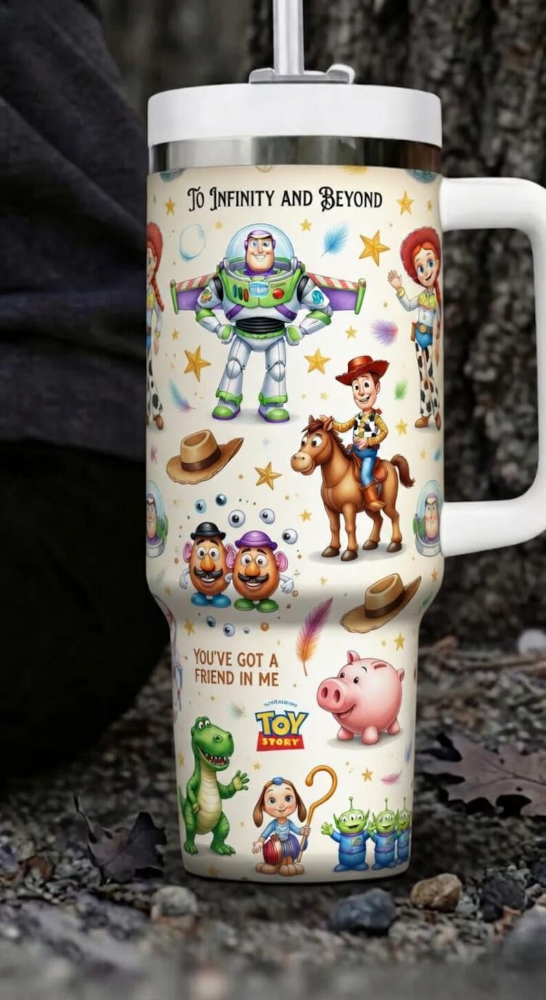 May include: A white travel mug featuring characters from the animated film "Toy Story." The design includes Buzz Lightyear, Woody, Jessie, and other characters, along with the phrases "To Infinity and Beyond" and "You've Got a Friend in Me."