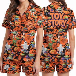 Puede incluir: Un conjunto de pijama de camisa de manga corta con botones y pantalones cortos a juego en naranja y negro. La tela presenta un patrón repetitivo de personajes de Toy Story, fantasmas, calabazas y telarañas. El texto TOY STORY está impreso.