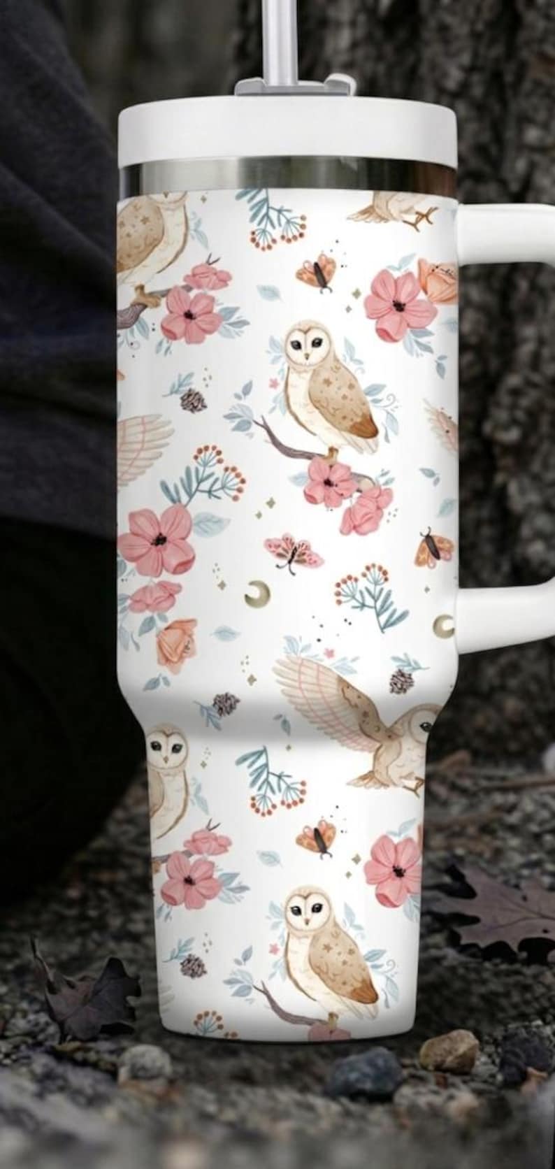 Puede incluir: Taza de viaje blanca con un patr&oacute;n repetido de b&uacute;hos, flores rosas y mariposas. La taza tiene un asa y una tapa blancas y est&aacute; dise&ntilde;ada para bebidas fr&iacute;as o calientes. El dise&ntilde;o tiene un tema caprichoso inspirado en la naturaleza.