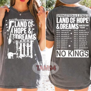 Puede incluir: Camiseta gris oscuro con el texto "SPRINGSTEEN & E STREET LAND OF HOPE & DREAMS AMERICAN TOUR" y un gráfico de un músico. La parte trasera de la camiseta muestra las fechas y lugares de la gira. El texto "NO KINGS" también es visible.