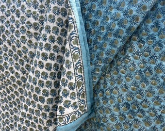 May include: A reversible quilted textile featuring a block-print pattern of small green floral motifs. One side has a white background, while the other side has a light blue background. A border with a repeating botanical design edges the fabric.