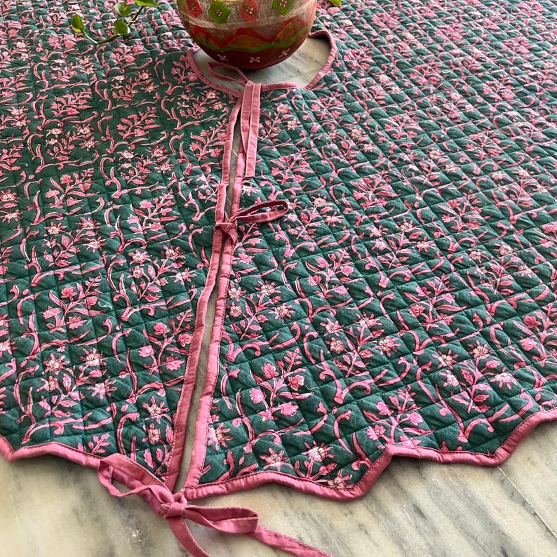 Puede incluir: Una falda de &aacute;rbol redonda y acolchada con un estampado floral rosa y verde. La falda tiene un borde festoneado y lazos rosas. El dise&ntilde;o floral se repite en toda la superficie, creando un aspecto decorativo y cohesivo.