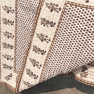 Peut inclure: Couverture crème avec un motif floral répété en marron et bordeaux. La couverture présente un motif cousu, une bordure marron et divers arrangements floraux. Fabriqué dans un matériau doux.