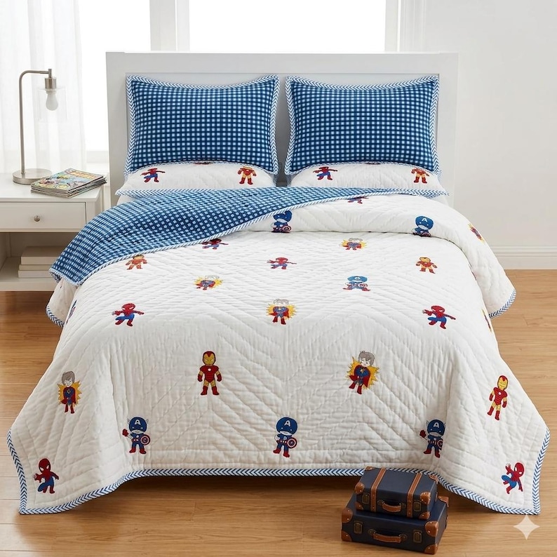 May include: A white quilt and two matching pillow shams featuring a repeating pattern of embroidered Marvel superhero characters. The bedding set includes a blue and white gingham check border and reverse side, with quilted chevron stitching.