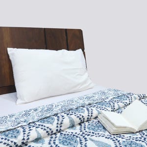 Könnte beinhalten: Ein weißes Kissen liegt an einem dunklen Holz-Kopfteil auf einem Bett mit einer blau-weiß gemusterten Steppdecke. Ein offenes Buch mit leeren Seiten liegt auf der Steppdecke. Die Steppdecke hat ein Blumenmuster.
