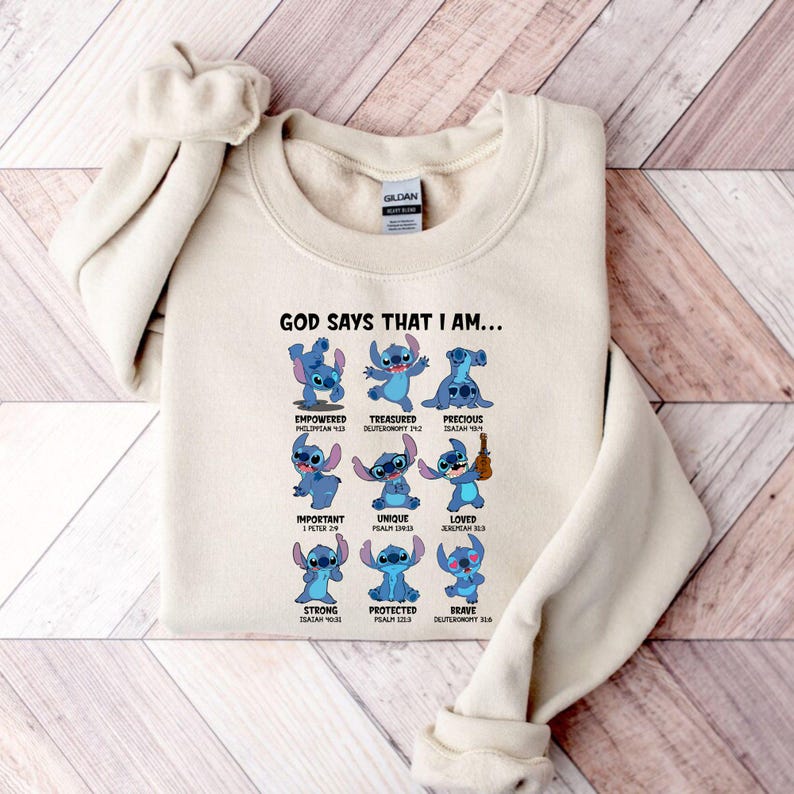Op de afbeelding: Een cr&egrave;mekleurige sweatshirt met een afbeelding van het personage Stitch uit Lilo & Stitch. Het ontwerp bevat Stitch in verschillende poses met woorden als "Empowered", "Treasured" en "Precious". De tekst "GOD SAYS THAT I AM..." staat bovenaan.
