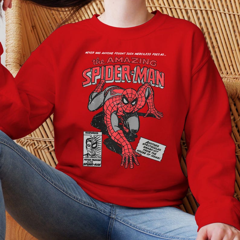 May include: A red sweatshirt featuring a comic book style graphic of Spider-Man. The graphic includes the text "the AMAZING SPIDER-MAN" and other comic book elements. The sweatshirt is a solid red color.