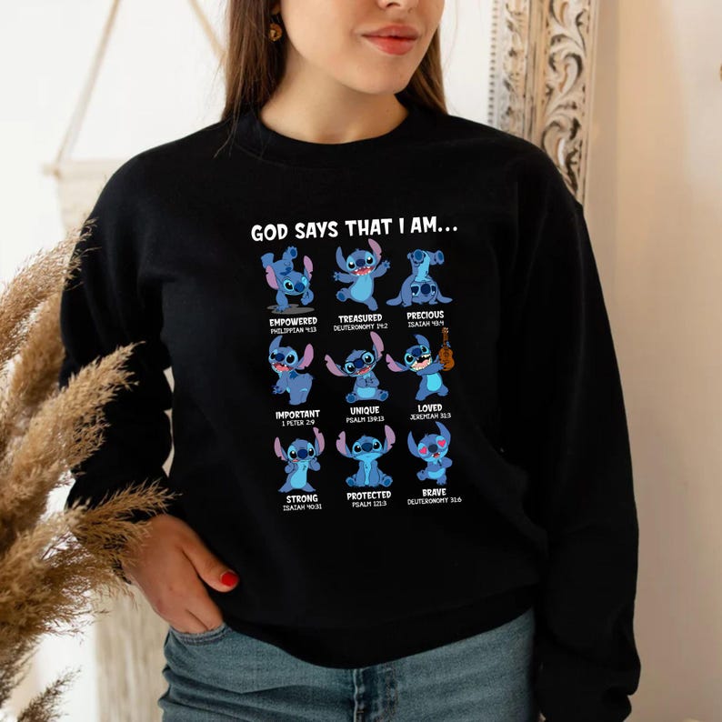Op de afbeelding: Zwart sweatshirt met een afbeelding van Stitch en de tekst "GOD SAYS THAT I AM..." samen met positieve woorden als "Empowered", "Treasured" en "Precious". Het ontwerp bevat blauwe Stitch-illustraties.