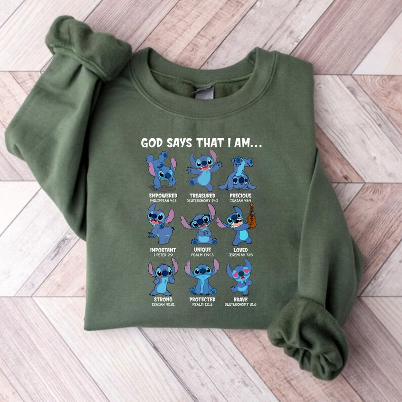 Op de afbeelding: Groen sweatshirt met de tekst "GOD SAYS THAT I AM..." en afbeeldingen van een blauw stripfiguur. Het personage wordt in verschillende poses getoond met woorden als "Empowered", "Treasured" en "Precious".