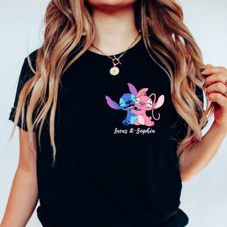 May include: Black t-shirt featuring a cartoon image of two characters hugging, one blue and one pink. The text "Lucas & Sophia" is printed in white below the image. The shirt has short sleeves and a round neckline.