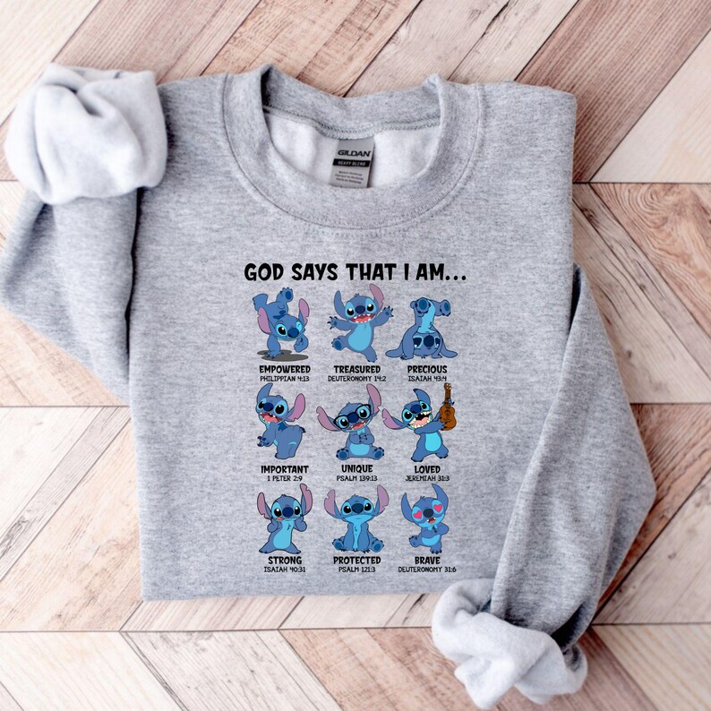 Op de afbeelding: Een lichtgrijs sweatshirt met een afbeelding van het personage Stitch. De tekst "GOD SAYS THAT I AM..." staat boven het personage, met woorden als "EMPOWERED", "TREASURED" en "PRECIOUS" onder elke afbeelding van Stitch.