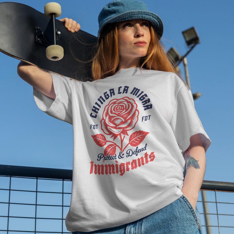 May include: White t-shirt with a red rose graphic and the text "Chinga La Migra" in blue, and "Protect & Defend Immigrants" in red. The shirt is a casual style.