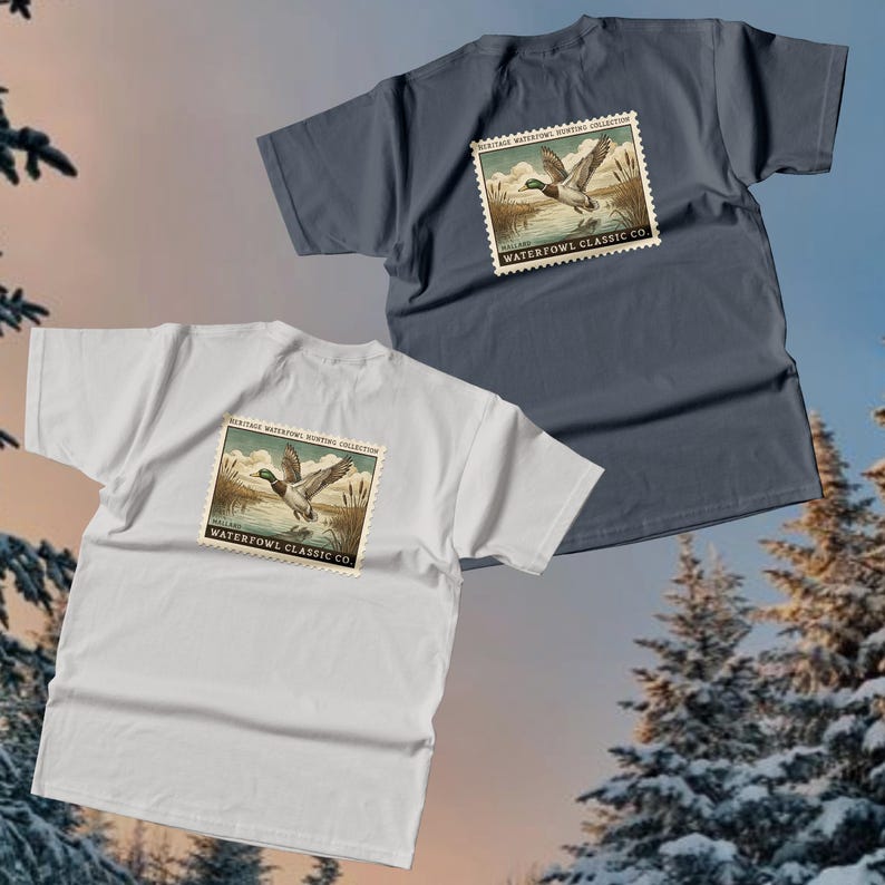 May include: Two t-shirts, one white and one dark blue, each featuring a vintage-style stamp design. The stamp depicts a duck in flight over water, with text reading "Heritage Waterfowl Hunting Collection" and "Waterfowl Classic Co."