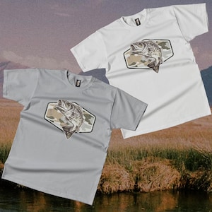 May include: Two short-sleeved t-shirts, one light grey and one white, with a graphic of a largemouth bass leaping from water. The fish is set against a camouflage background within a hexagonal shape. The shirts are casual wear.