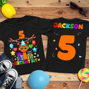 May include: Black t-shirts with a colorful birthday design. One shirt features a large orange number 5, the text "BIRTHDAY BOY," and cartoon characters. The other shirt has the name "JACKSON" and the number 5.