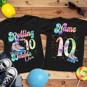 May include: Two black t-shirts with colorful graphics. One says "Rolling into 10 Double Digits" with roller skates. The other says "Name 10" with roller skates. Accessories include sunglasses, a lollipop, a blue balloon, and a pineapple.