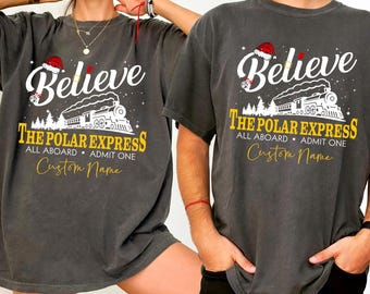 May include: Two dark gray t-shirts with the text "Believe" and "The Polar Express" in white and gold. The design includes a train, Santa hat, and the words "All Aboard, Admit One" and "Custom Name".