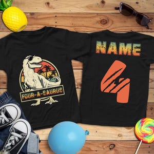 May include: Black t-shirts with dinosaur graphics. One shirt features a dinosaur wearing sunglasses with the text "FOUR-A-SAURUS". The other shirt has the number "4" and the word "NAME".
