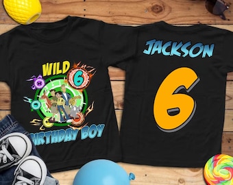 May include: Two black t-shirts with vibrant graphics. One displays "WILD 6 BIRTHDAY BOY" with cartoon characters. The other has the name "JACKSON" and the number "6".