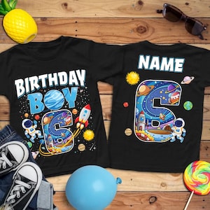 May include: Black t-shirts with a space-themed design. One shirt says "BIRTHDAY BOY" with a number "6" and a rocket ship. The other shirt has the word "NAME" above a number "6" with planets and an astronaut.