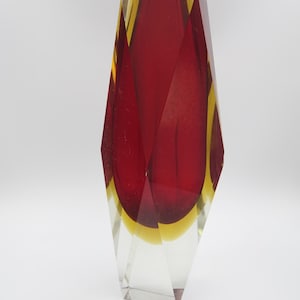 May include: A faceted glass vase with a striking design. The vase features a clear, geometric exterior with a vibrant interior of red and yellow hues. The vase's shape is tall and angular, showcasing a modern aesthetic.