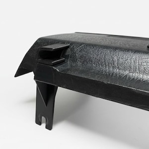 Può includere: Un componente interno per auto in plastica nera caratterizzato da una finitura superficiale testurizzata e granulosa. Il pezzo include una sezione superiore rigida e angolata con una staffa di montaggio sporgente e un braccio di supporto.