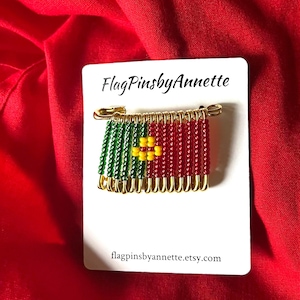 May include: A pin featuring a flag design made of gold-toned safety pins strung with green, red, and yellow beads. The pin is attached to a white display card printed with the text FlagPinsbyAnnette and flagpinsbyannette.etsy.com.