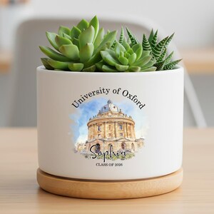 May include: A white ceramic planter with a wooden base, featuring a succulent plant. The planter is decorated with the words "University of Oxford" and a watercolor image of a building. The name "Sophia" and "Class of 2026" are also displayed.
