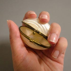 Open vintage clam shell jewelry box in hand, mother of pearl trinket box with brass trim and clasp