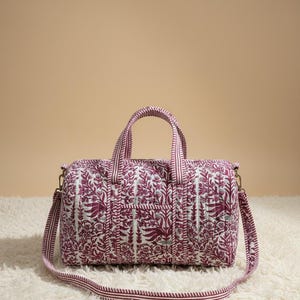 May include: A quilted travel bag with a floral pattern in shades of burgundy and white. The bag has a rectangular shape with a top handle and a detachable shoulder strap. The bag measures approximately 10 inches in length, 6 inches in height, and 6 inches in width.