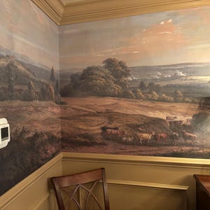 Puede incluir: Un mural de pared que presenta una pintura de paisaje pastoral con colinas, &aacute;rboles y una manada de ganado pastando en un campo. La escena est&aacute; representada en tonos tierra apagados con un cielo suave. Un termostato rectangular blanco est&aacute; montado en la pared.