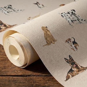 Op de afbeelding: Een rol beige behang met aquarel illustraties van verschillende hondenrassen, waaronder een Dalmatische hond, Golden Retriever en Duitse Herder. De honden worden in verschillende poses afgebeeld, wat een speels element aan het ontwerp toevoegt. Het behang heeft een getextureerde uitstraling.