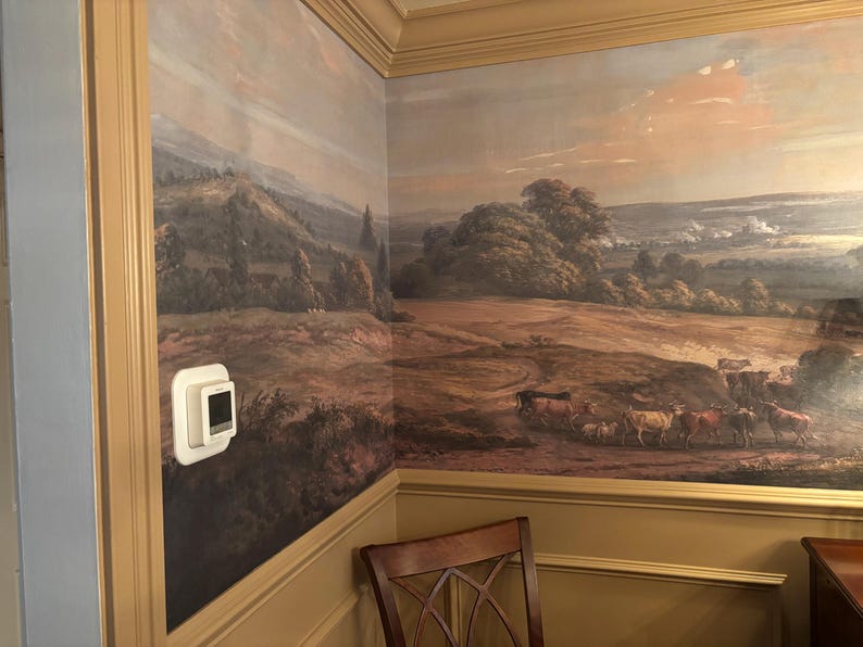 Puede incluir: Un mural de pared que presenta una pintura de paisaje pastoral con colinas, &aacute;rboles y una manada de ganado pastando en un campo. La escena est&aacute; representada en tonos tierra apagados con un cielo suave. Un termostato rectangular blanco est&aacute; montado en la pared.