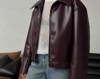 以下が含まれることがあります： 襟付きとジッパーフロントのバーガンディフェイクレザージャケット。 ジャケットは少しオーバーサイズフィットで、リブ編みの裾と袖口が特徴です。 モデルは白いセーターとブルージーンズを着用しています。 ジャケットはスタイリッシュなアウターウェアです。