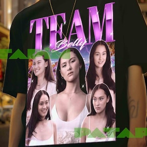 Peut inclure: T-shirt noir avec l'inscription "TEAM Belly" en violet et blanc. Le t-shirt présente des images de plusieurs femmes. L'arrière-plan montre une scène de ville.