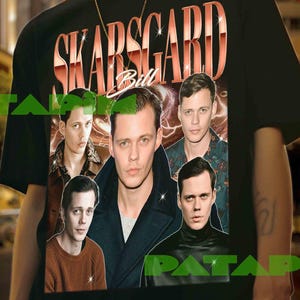 Puede incluir: Camiseta negra con el nombre "SKARSGARD" en color cobre y el nombre "Bill" debajo. La camiseta muestra múltiples imágenes de una persona. El fondo es una escena de calle urbana.