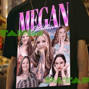 May include: Black t-shirt featuring a graphic of the name "Megan Stalter" in pink and white, with images of the actress. The shirt is worn by a person with a gold chain necklace and a bracelet.