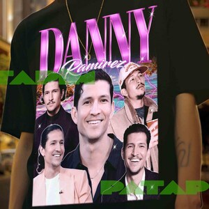 May include: Black t-shirt featuring a collage of images of Danny Ramirez, with the name "Danny Ramirez" in a pink and purple font. The shirt has a vintage, retro design, with a cityscape background.