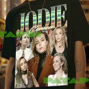 Peut inclure: T-shirt noir avec le nom "JODIE COMER" dans une police rétro irisée. Le t-shirt présente plusieurs images d'une femme. L'arrière-plan est un paysage urbain flou.