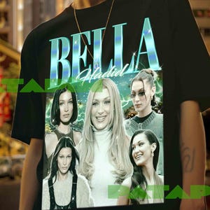 Peut inclure: T-shirt noir avec l'inscription "BELLA Hadid" en bleu sarcelle et blanc. Le t-shirt présente plusieurs images de Bella Hadid. Le modèle porte une chaîne dorée.